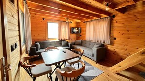 Un interior acogedor de cabaña con detalles de madera, un conjunto de sofá, una mesa de comedor con sillas y un televisor montado en la pared.