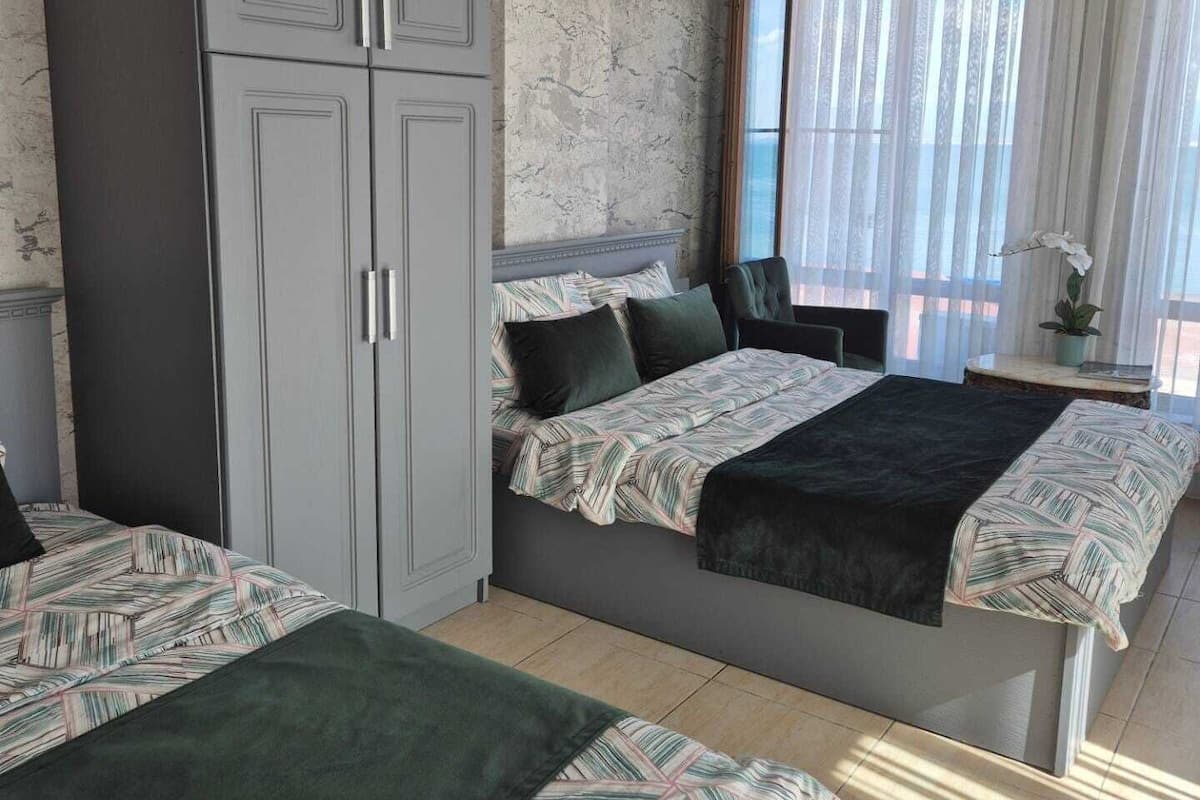 A bedroom with two beds, a wardrobe, a window with curtains, and a hanging light fixture.