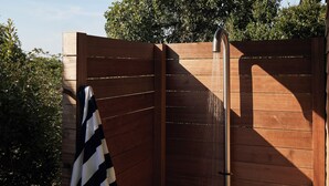 Une clôture en bois avec une pomme de douche, une serviette suspendue sur le côté gauche et de la verdure en arrière-plan.