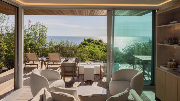 Un espace extérieur moderne aménagé avec des sièges confortables, offrant une vue sur l’océan et comprenant des fauteuils et une table.