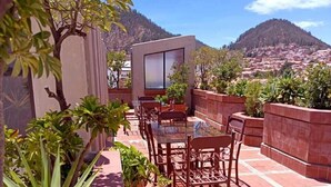 Una terrazza con tavolo e sedie, circondata da piante in vaso e vista su un paesaggio montuoso.