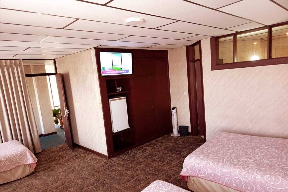 Quarto de hotel com duas camas, televisão, escrivaninha e janela.