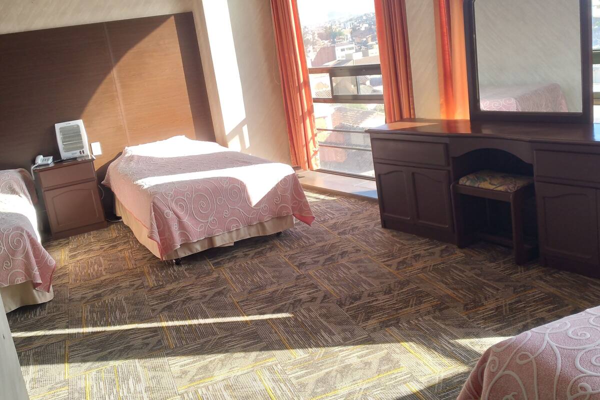 Quarto de hotel com cama, mesa de cabeceira com telefone, espelho e cômoda.