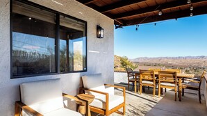 Une terrasse couverte avec des sièges d’extérieur, de grandes fenêtres et une vue sur les montagnes.