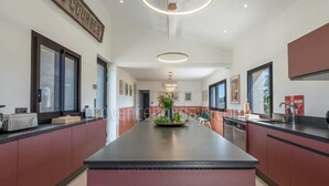 Una cocina moderna con una isla central, encimeras oscuras y muebles lacados rojos. Se observan cuadros en las paredes y un ventanal que proporciona luz natural.
