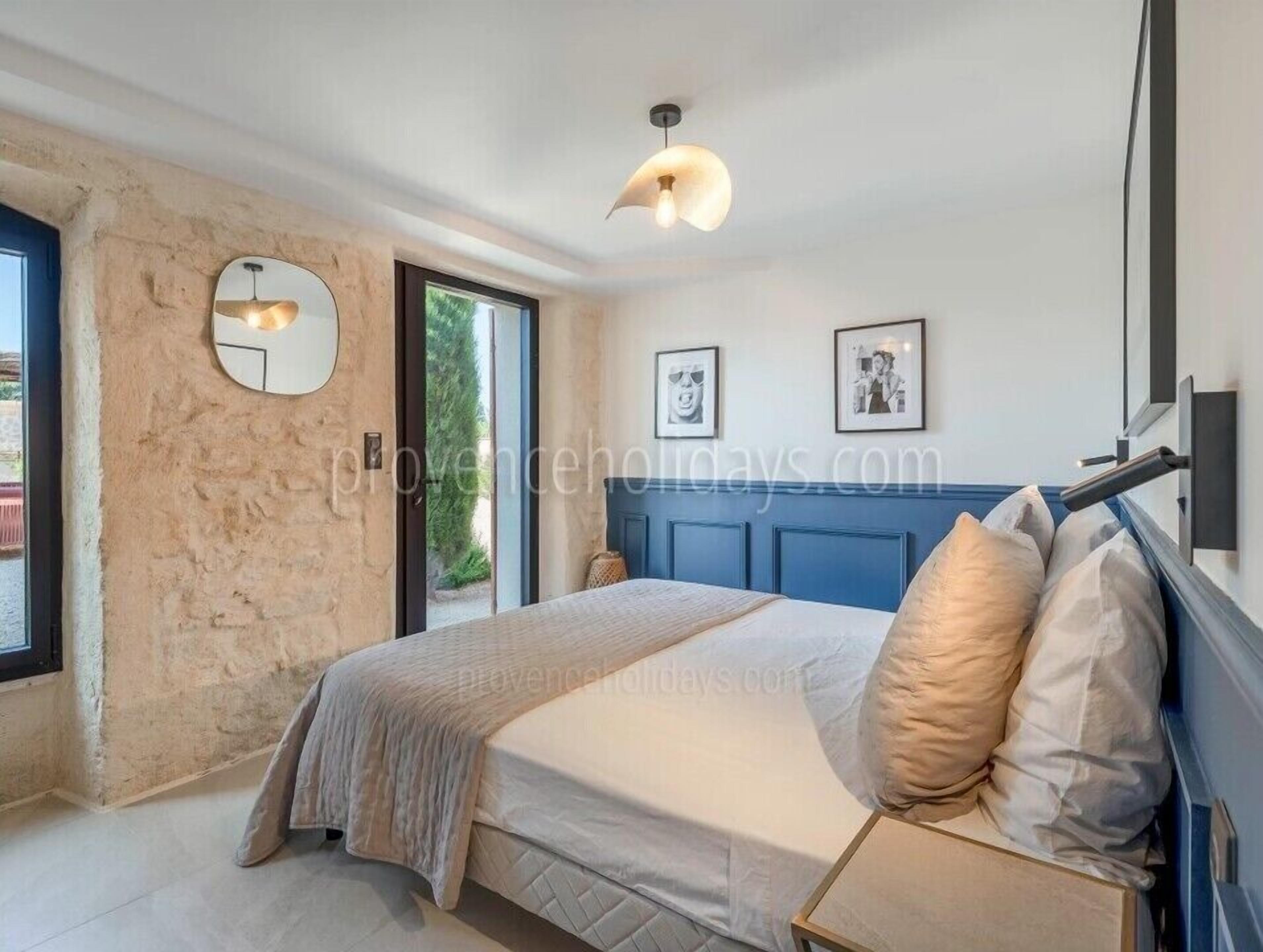 A bedroom with a stone wall, a bed with a headboard, a round mirror, and two framed pictures on the wall.