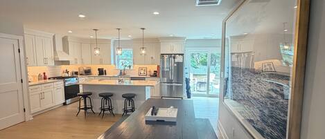 A modern kitchen with white cabinets, a central island, bar stools, and pendant lighting.