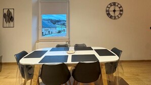 Un comedor con una mesa redonda, sillas negras, un reloj en la pared y una ventana con vistas a un paisaje nevado.
