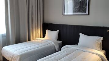 Habitación de hotel con dos camas individuales, un cabecero oscuro, un cuadro enmarcado en la pared y una ventana con cortinas.