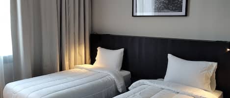A hotel room with two single beds, a dark headboard, a framed picture on the wall, and a window with curtains.