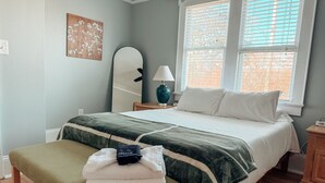 A bedroom with a bed, bench, lamp, and artwork.