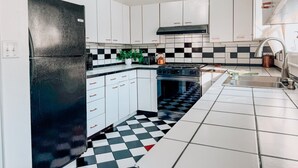 A kitchen with white cabinets, a black refrigerator, a checkered floor, and a stove.