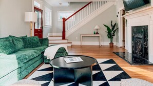 A living room with a green sofa, a round coffee table, a fireplace, and a staircase.