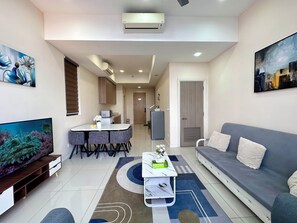 A modern living room with a grey sofa, a TV, and a dining area with a table and chairs. - Spacious Duplex Oasis Icon City (Petaling Jaya)