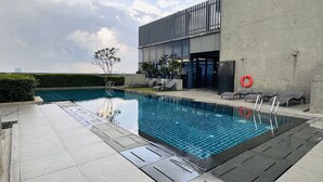 Una piscina moderna al aire libre con solárium de azulejos, sillas de descanso y un edificio con amplias ventanas.