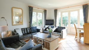 A living room with a sofa set, a coffee table, a TV, and a dining area with chairs. - Holiday Home Near Beach and Forest (Sint Maartensvlotbrug)
