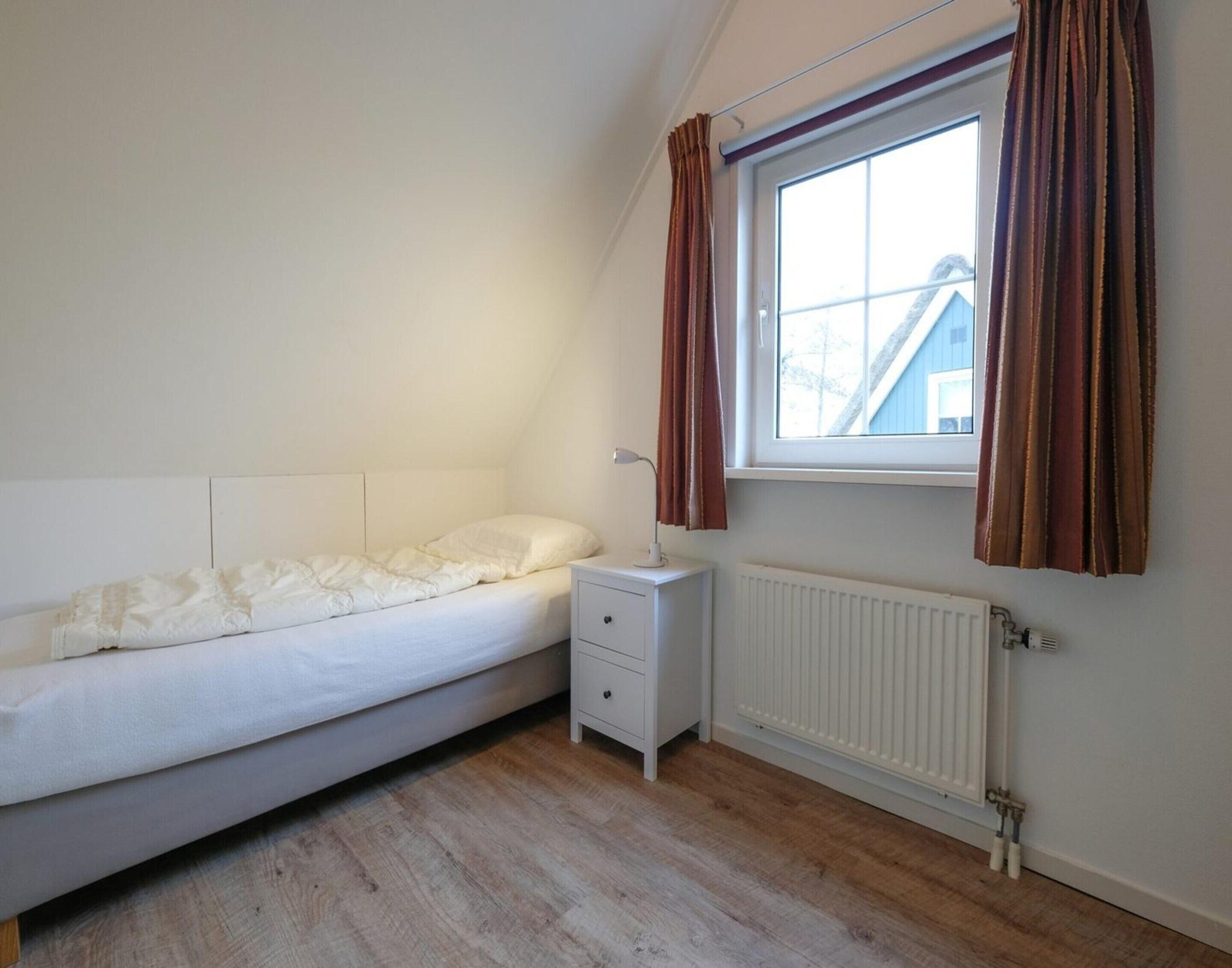 A bedroom with a single bed, a nightstand, a window with curtains, and a radiator.