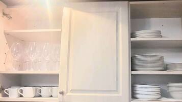 Una cocina con armarios abiertos que exhiben tazas blancas, vasos y platos y tazones apilados.