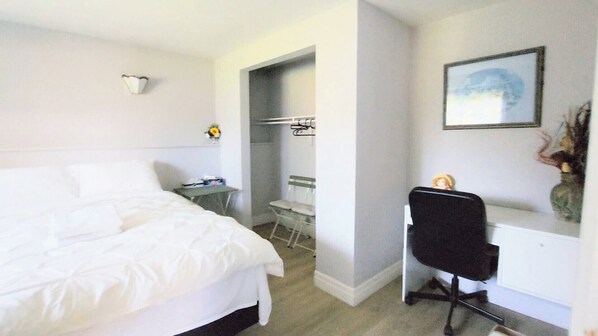 Habitación de hotel con cama, escritorio y silla. Hay un armario y una mesita con un jarrón de flores.