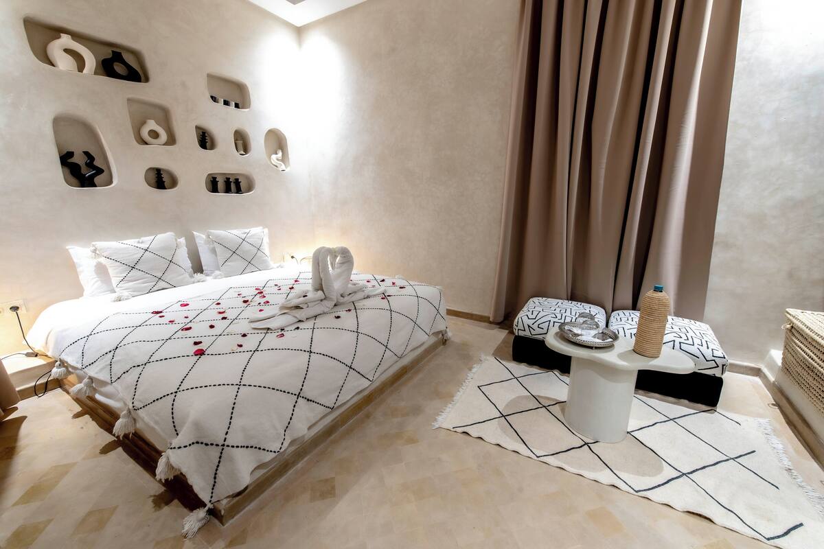Une chambre moderne avec un grand lit, une table de chevet avec une lampe et un mur orné de motifs décoratifs.