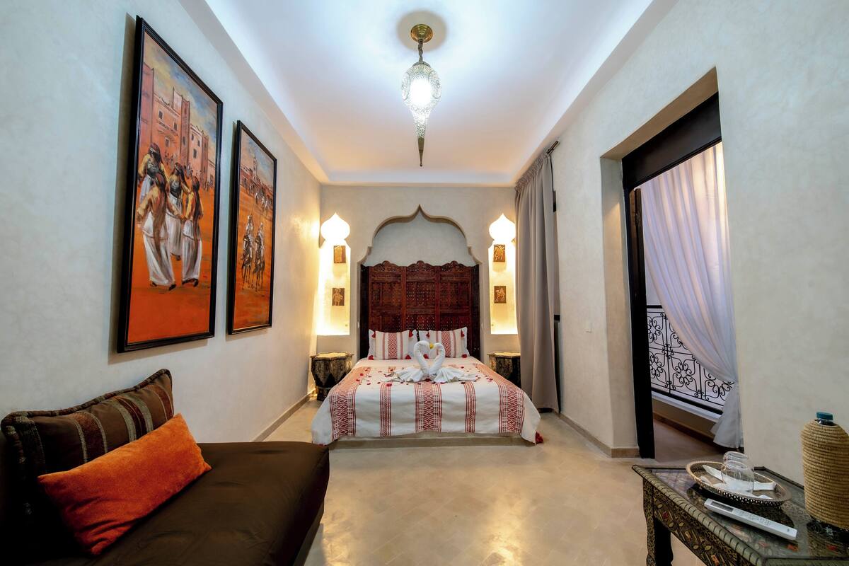 Une chambre d’hôtel comprenant un lit, un canapé, une table de chevet, une lampe et un élément décoratif mural.