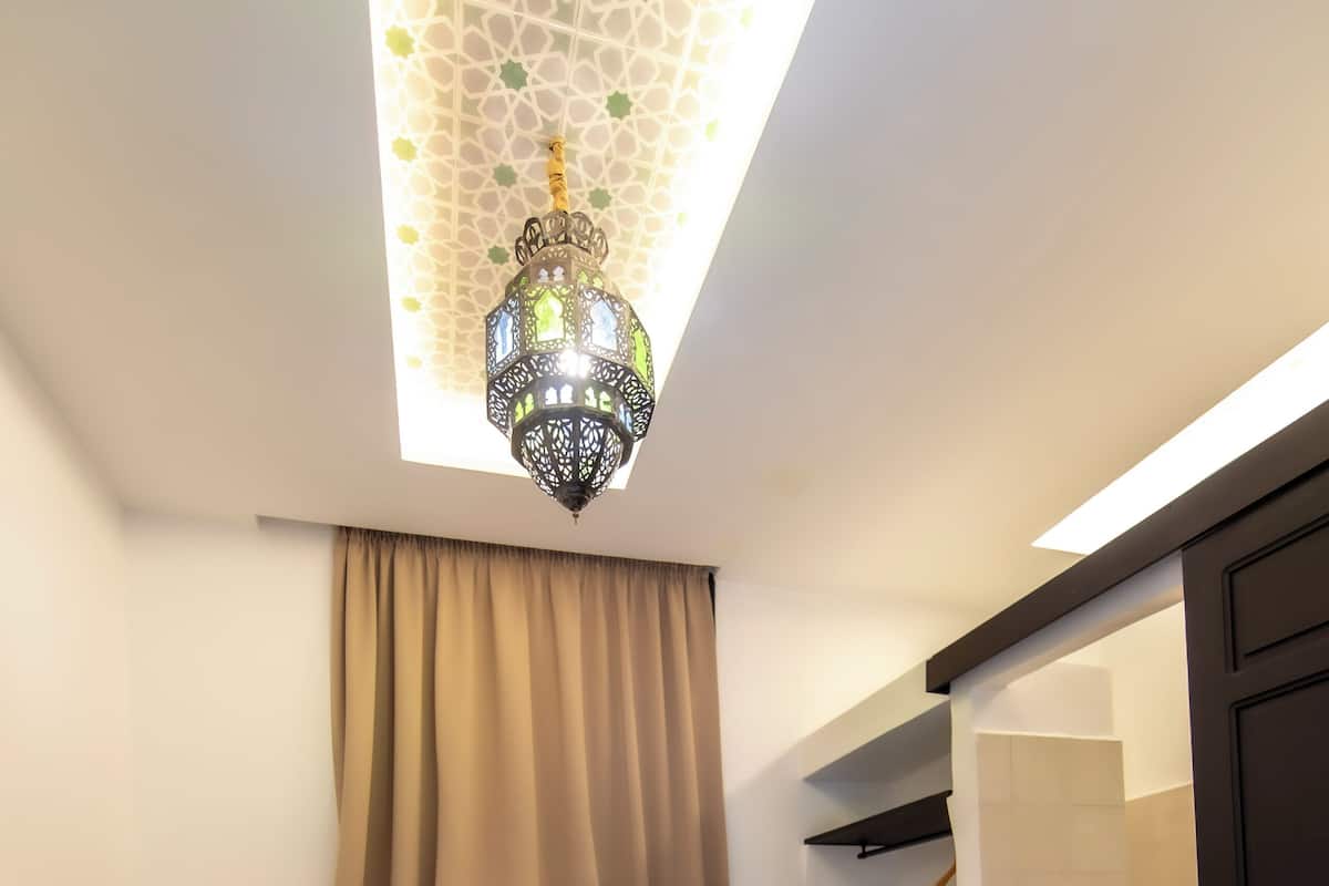 Une chambre d’hôtel comprenant un lit, une table de chevet, une lampe, un luminaire suspendu, une porte de salle de bain et un espace douche.