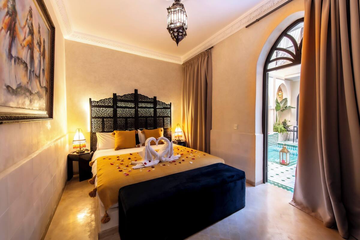 Une chambre d’hôtel comprenant un lit, une table de chevet, une lampe, une tête de lit décorative et une vue sur l’extérieur.