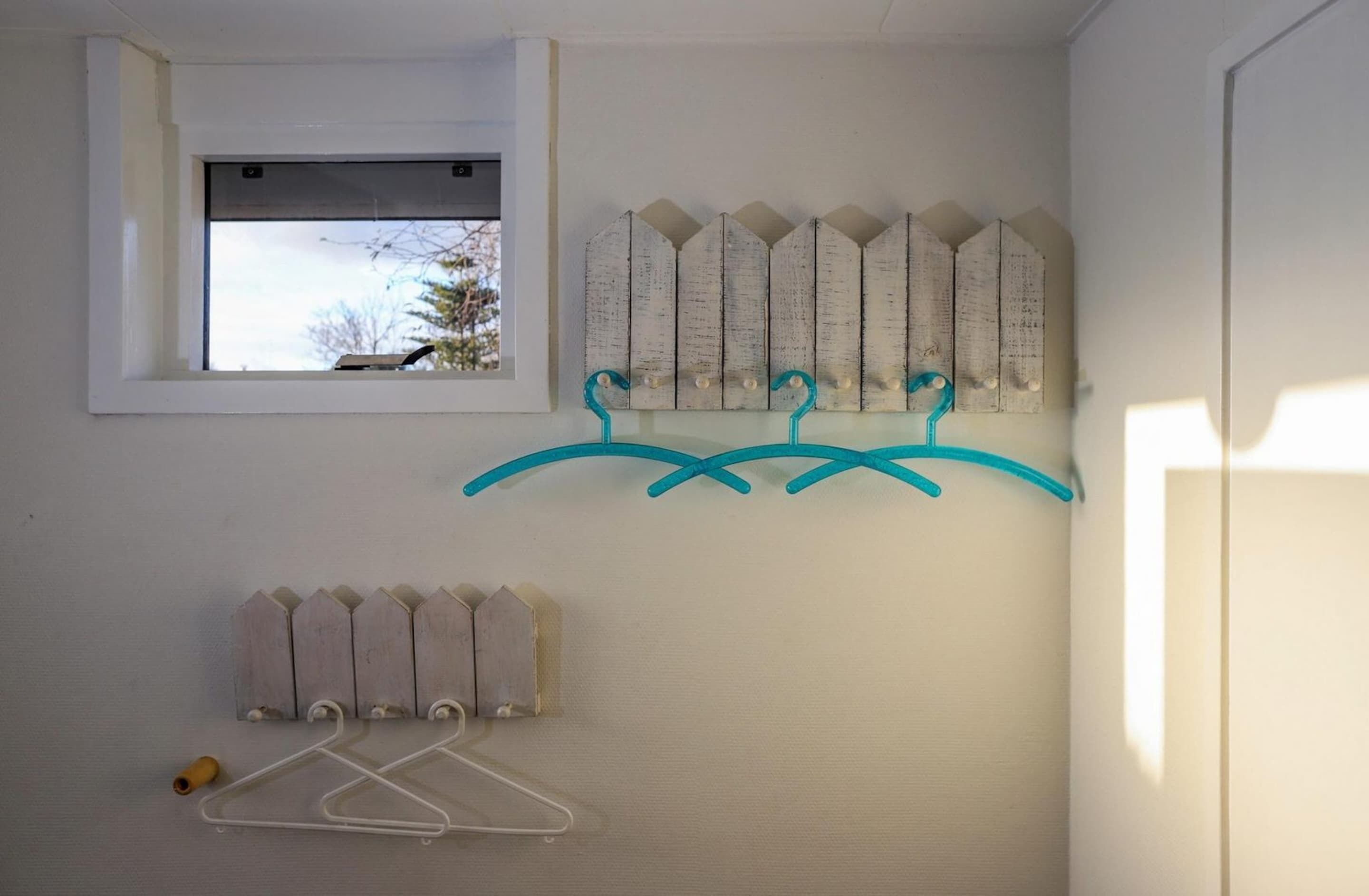 Um quarto com janela, um varal fixado na parede e um painel de madeira na parede.