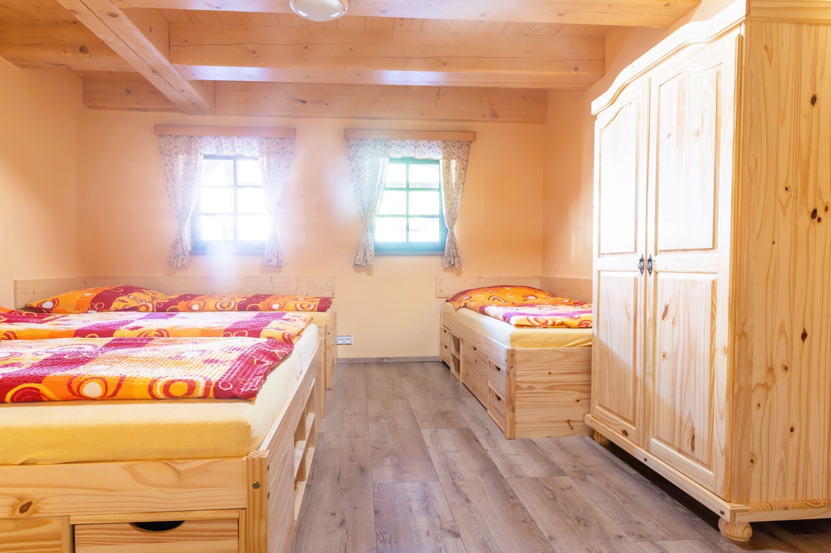 Una habitación con dos camas de madera, un armario y dos ventanas con cortinas.
