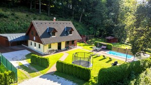 Une maison dotée d’un grand jardin, comprenant une piscine, un trampoline et un espace de jeux clôturé.