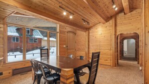 Ein Holzinterieur mit einem großen Esstisch, Stühlen und Blick auf eine verschneite Landschaft durch große Fenster.