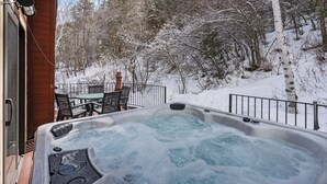 Ein Whirlpool auf einer Holzterrasse mit Blick auf einen verschneiten Wald.