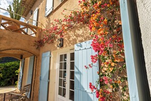 Un bâtiment doté d’un balcon en bois, d’une fenêtre avec des volets et d’un mur recouvert de plantes grimpantes en fleurs.