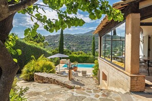 Une terrasse en pierre avec une piscine, du mobilier d’extérieur et une vue sur une colline.