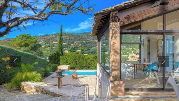 A stone patio with a pool, outdoor furniture, and a view of a hilly landscape.