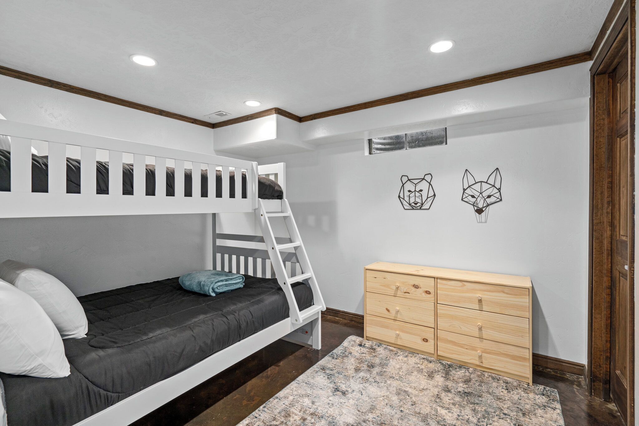 Una cama litera con escalera, un aparador de madera y dos elementos decorativos en la pared.