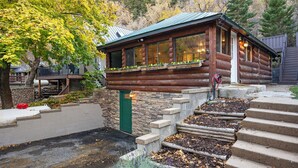 Une cabane en rondins avec des fondations en pierre, une terrasse en bois et une porte verte.