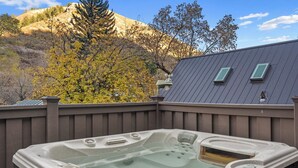 Un bain à remous installé sur une terrasse en bois, avec une montagne et des arbres en arrière-plan.