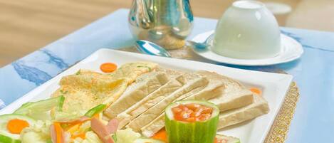 A plate of food with bread, vegetables, and a tomato. There is a teapot and a cup on the table.