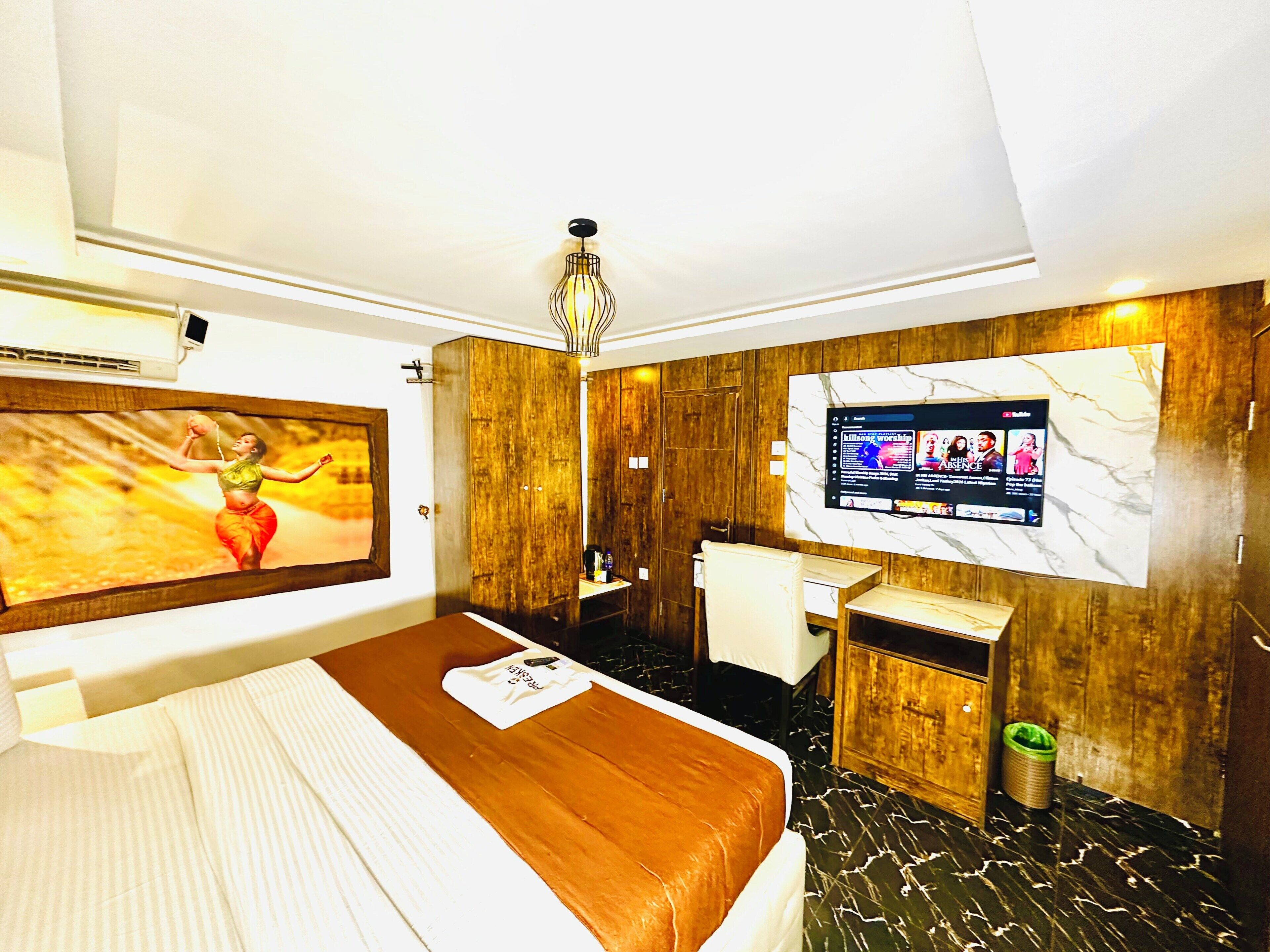 A hotel room with a bed, a desk, a television, and a wall-mounted air conditioning unit.