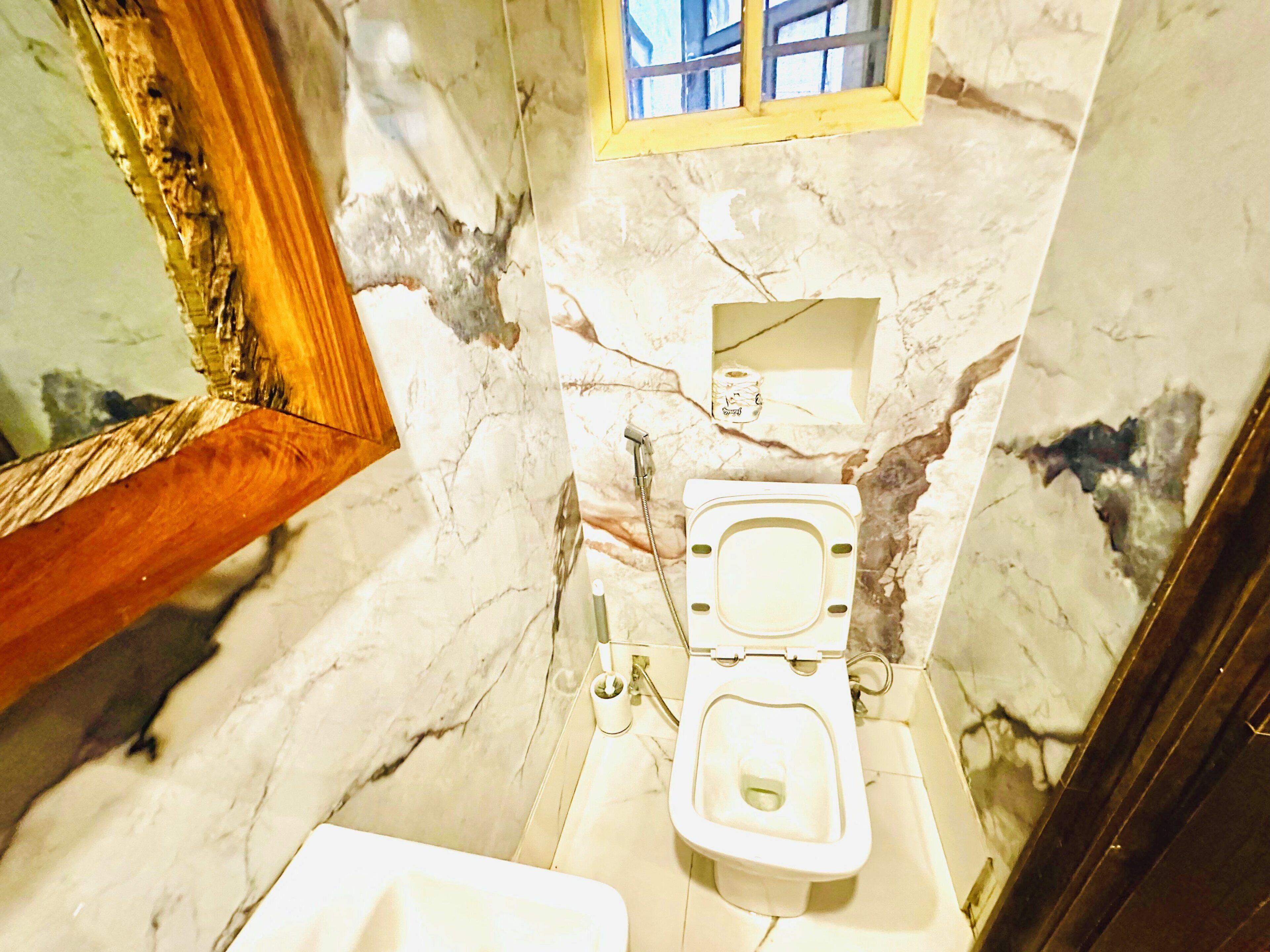 Un baño con pared de mármol, inodoro, lavamanos y espejo.