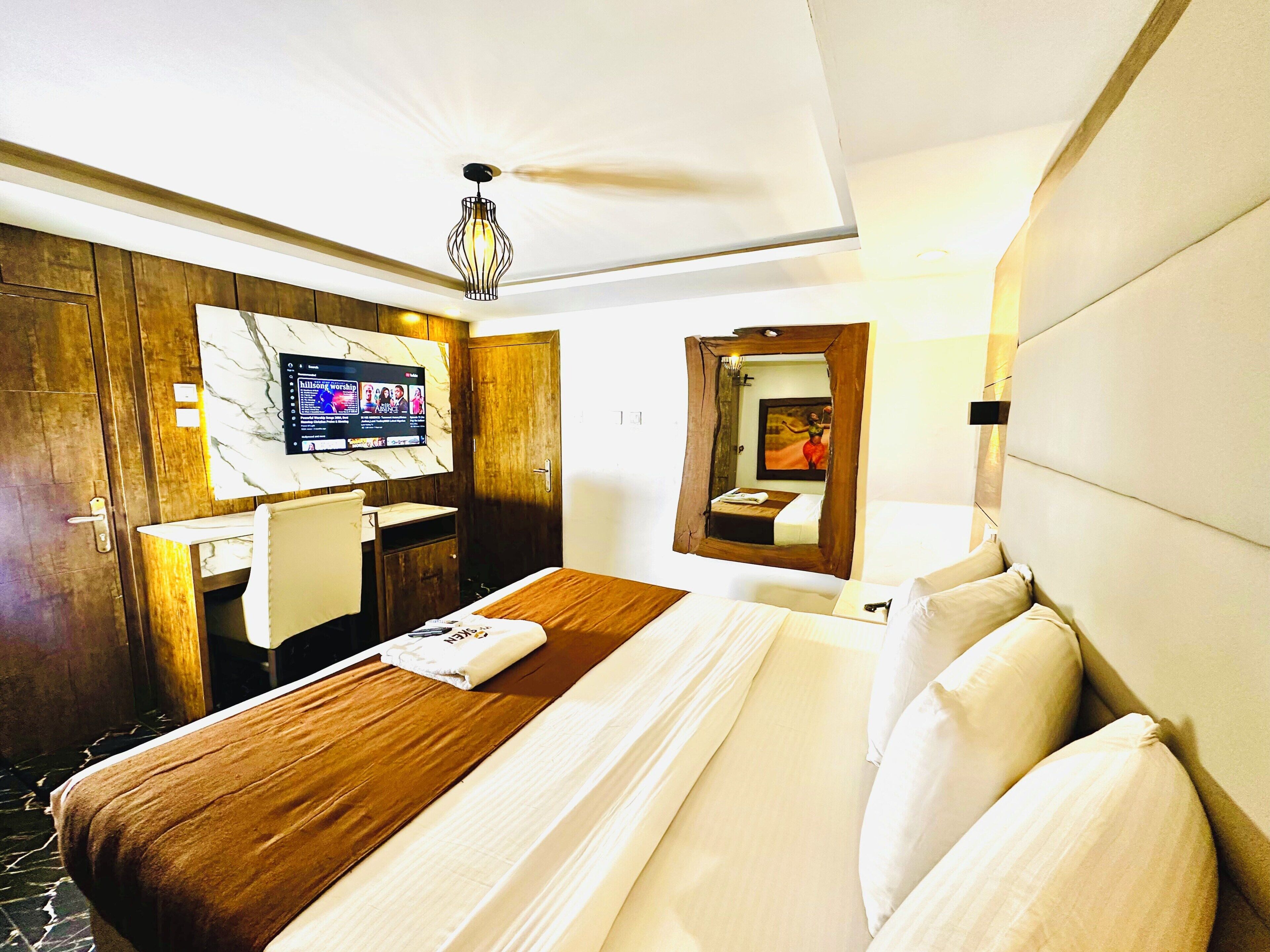 A hotel room with a bed, a desk, a television, and a mirror.