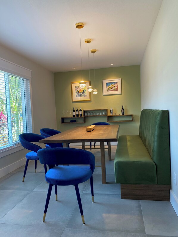 Un espace repas avec une table en bois, des chaises bleues, un banc vert et des luminaires suspendus.