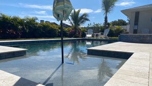Piscina com água cristalina, rodeada por azulejos de pedra e palmeiras.