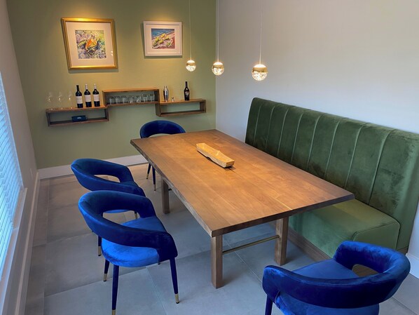 Un comedor con una mesa de madera, sillas azules, un banco acolchado verde y obras de arte en las paredes.
