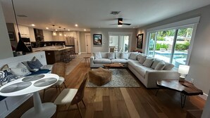 Una sala de estar moderna con comedor, una cocina al fondo y ventanas amplias que ofrecen vistas al exterior.