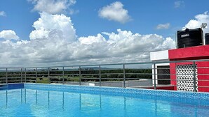 Une piscine aux carreaux bleus, entourée d’une clôture métallique, et un bâtiment rouge avec un réservoir d’eau en arrière-plan.