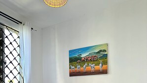 Une chambre à coucher avec un lit en bois, du linge de lit blanc, un tableau représentant des animaux sauvages, une fenêtre donnant sur un paysage agréable et un panier en osier.