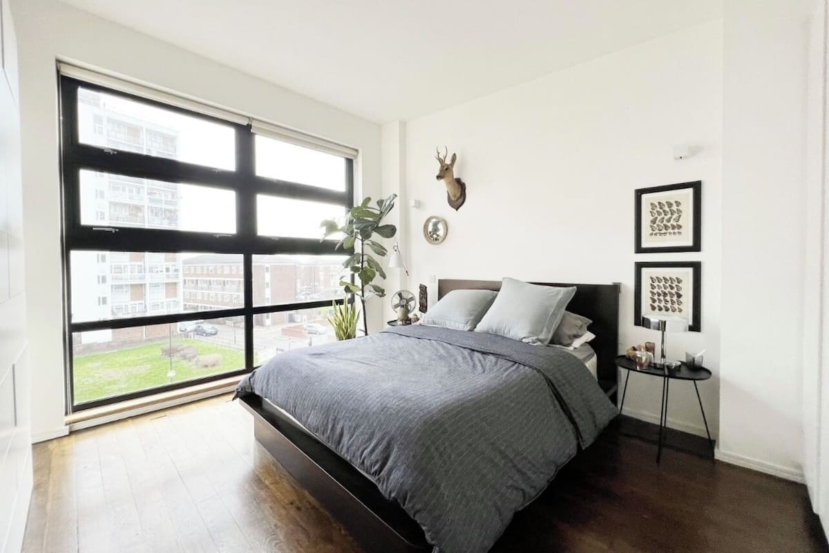 A bedroom with a large window, a bed, a wall-mounted deer head, and framed artwork.