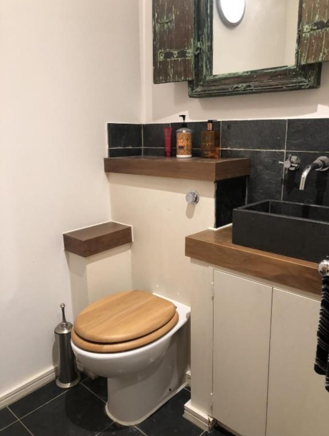 A bathroom with a wooden toilet, a black sink, and a mirror above the mirror cabinet.